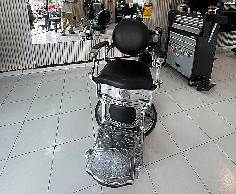 Silla de barbero cromada con asiento negro junto a la caja de herramientas.